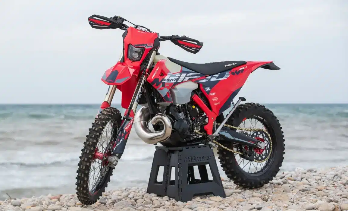 Rote Rieju MR 300i PRO 2027 Enduro auf einem Steinufer vor dem Meer, Seitenansicht.