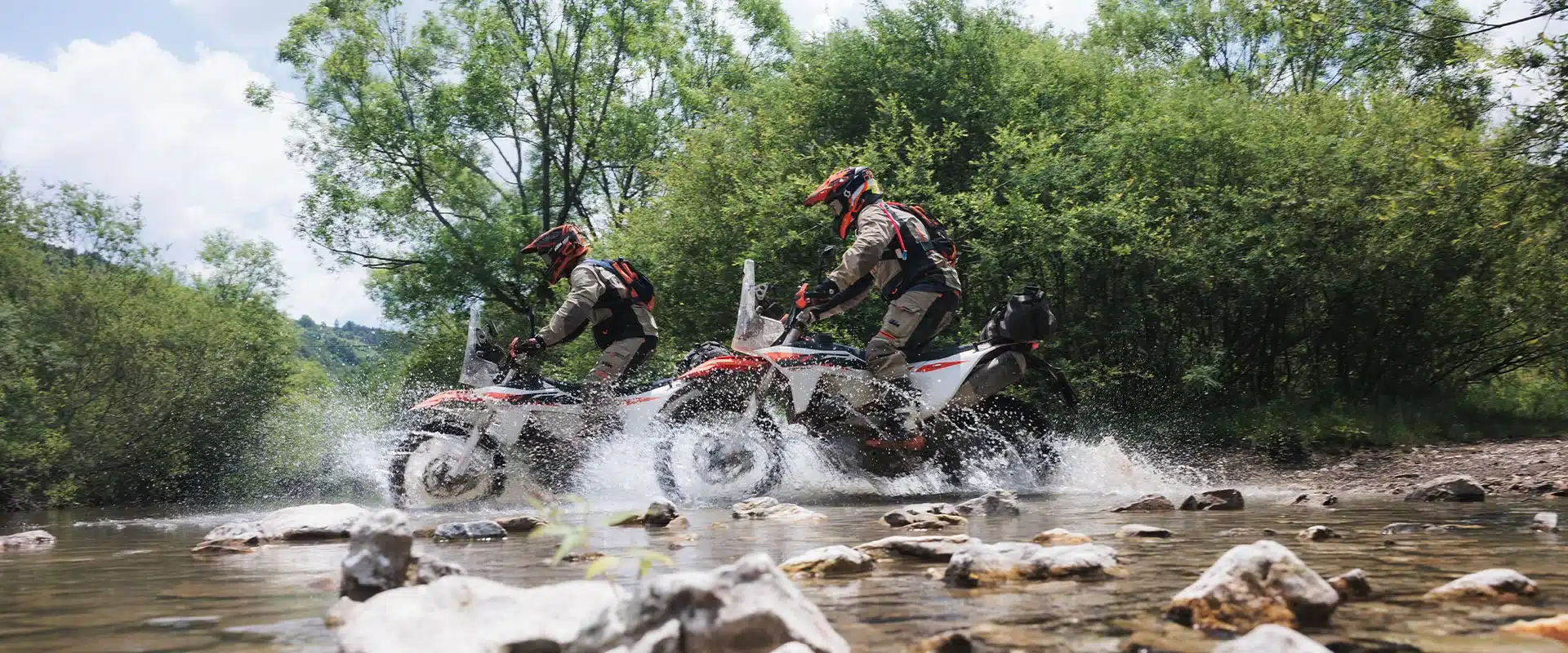 KTM 690 RALLY Motorräder mit Fahrern überqueren einen flachen Fluss in offener Landschaft.