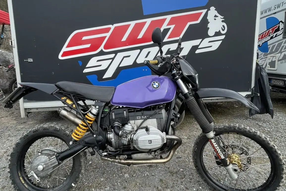Seitenansicht des SWT-SPORTS EnduroBoxer Nr. 150, einem modifizierten BMW R 80 G/S Motorrad mit lila Tank und Geländebereifung vor einem SWT-SPORTS Anhänger.