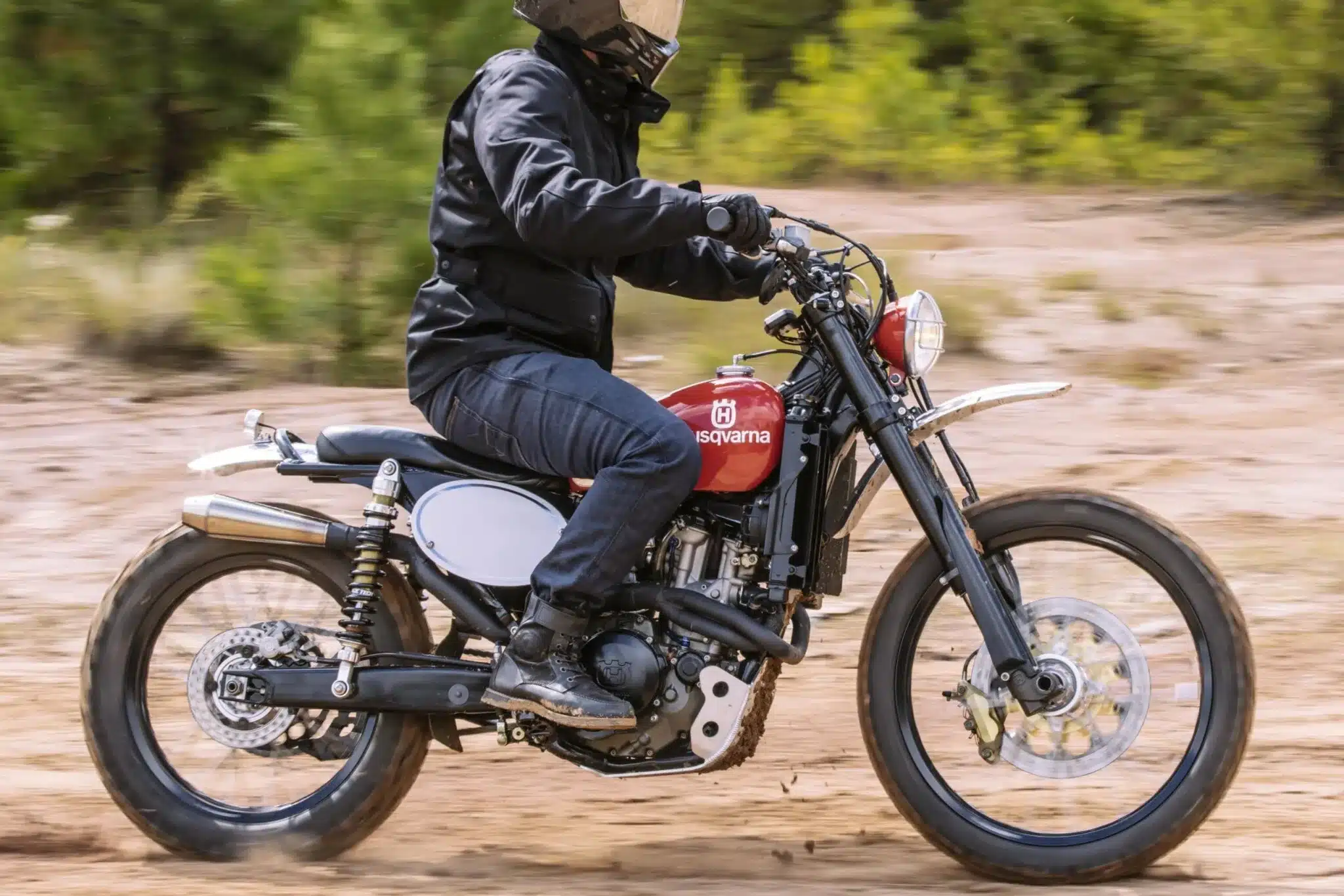 Motorradfahrer auf einer klassischen Husqvarna mit rotem Tank und Doppelfederbein-Heck im Gelände