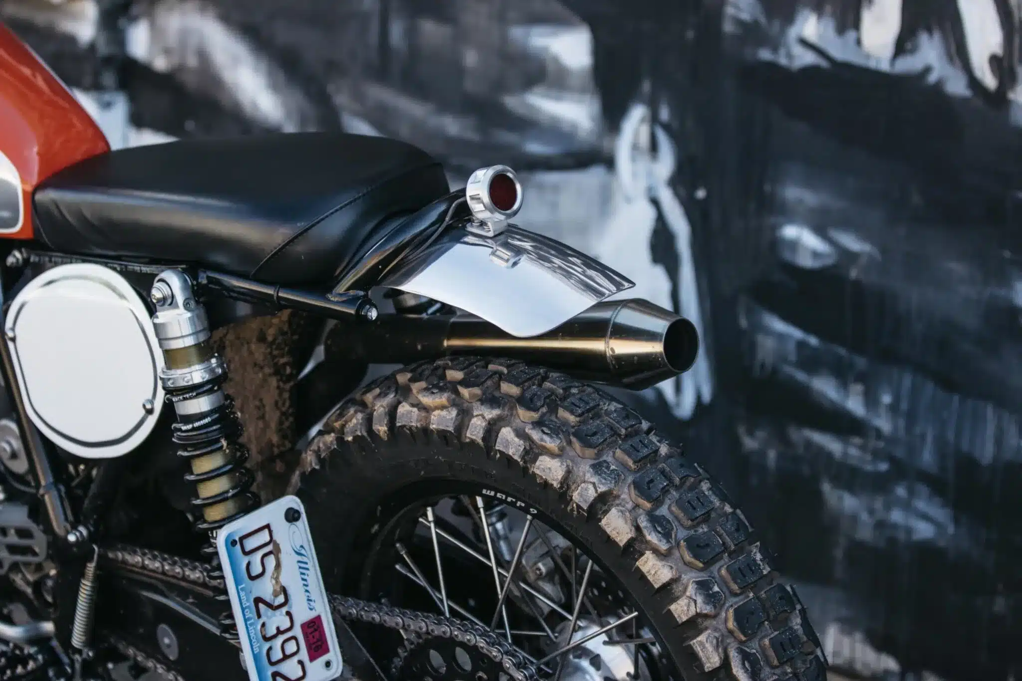 Motorrad-Heck mit Chromkotflügel, dickem Enduro-Reifen und Twin-Shock-Federbein, Nahaufnahme von Sitz, Auspuff und Kennzeichen.