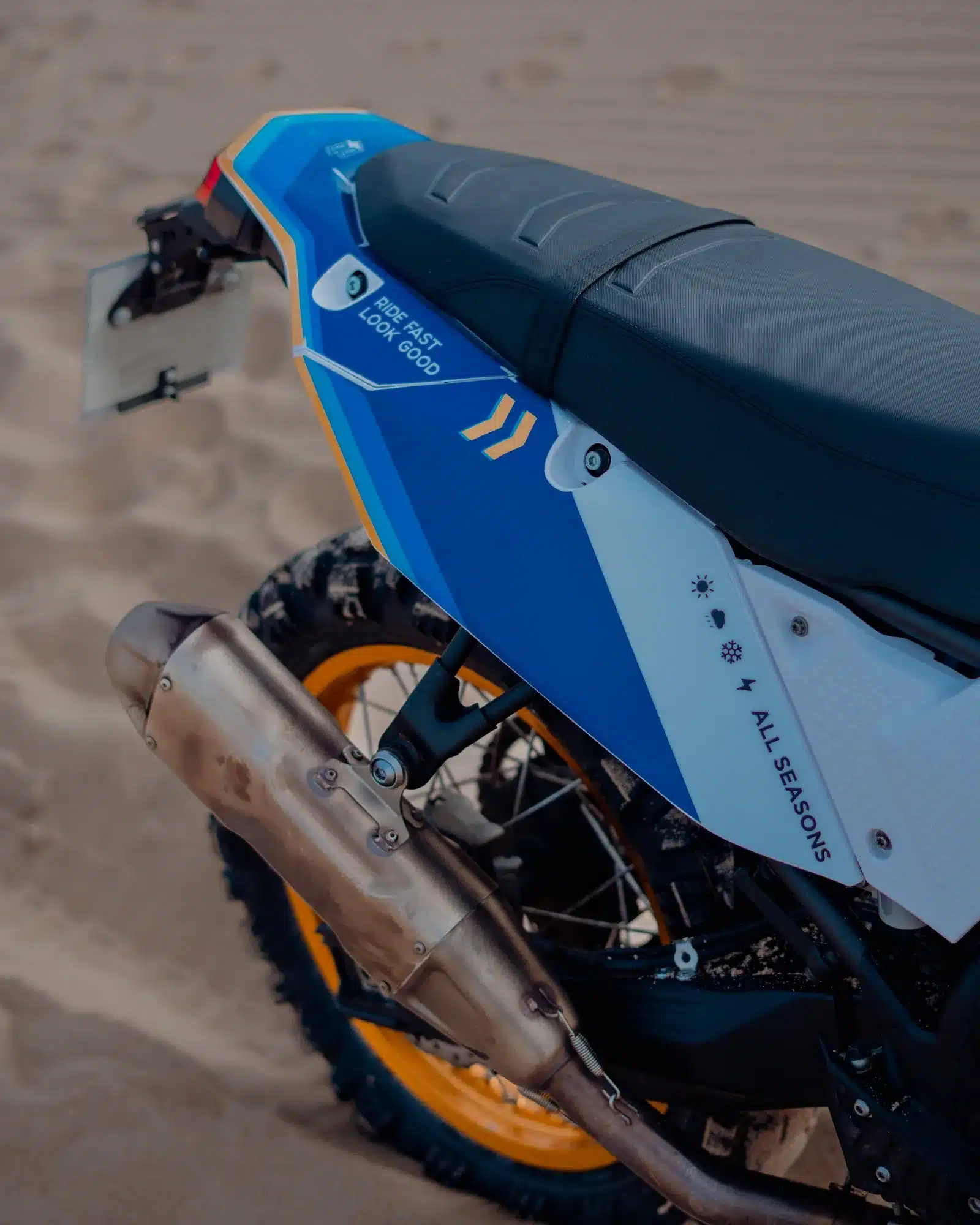 Detailfoto vom Heck einer Yamaha Ténéré 700 mit Umbau-Kit, montiertem Auspuff und auffälligen blauen Verkleidungsteilen im Sand