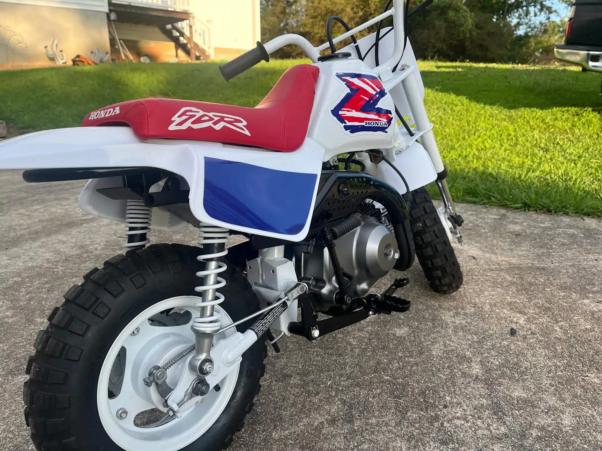 Restaurierte Honda Z50 aus dem Jahr 1995 mit weiß-blau-rotem Dekor, originalem Tank und 49-ccm-Einzylindermotor, Seitenansicht auf Betonfläche.