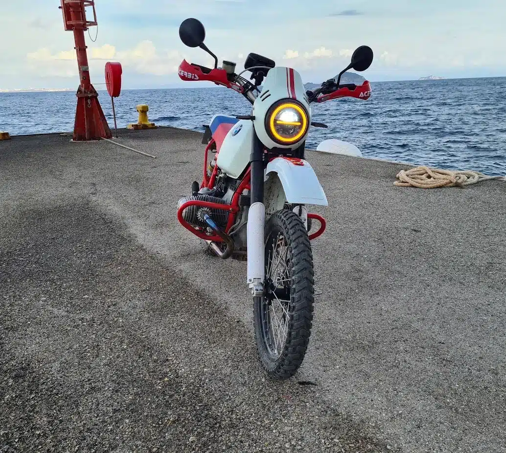 Frontansicht eines SWT-SPORTS BMW Boxer Umbaus mit rot verstärktem Rahmen, USD-Gabel und Endurobereifung auf einem Pier am Meer.