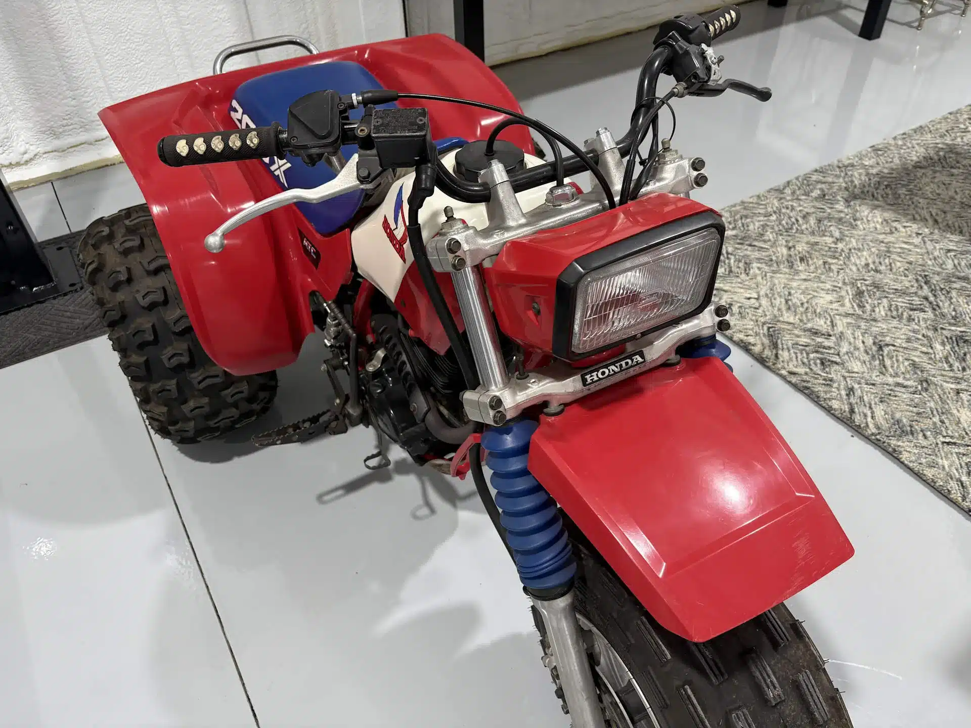 Honda ATC 200X Dreirad von 1985, Ansicht schräg von vorne mit roter Verkleidung, blauem Sitz und grobstolligen Reifen