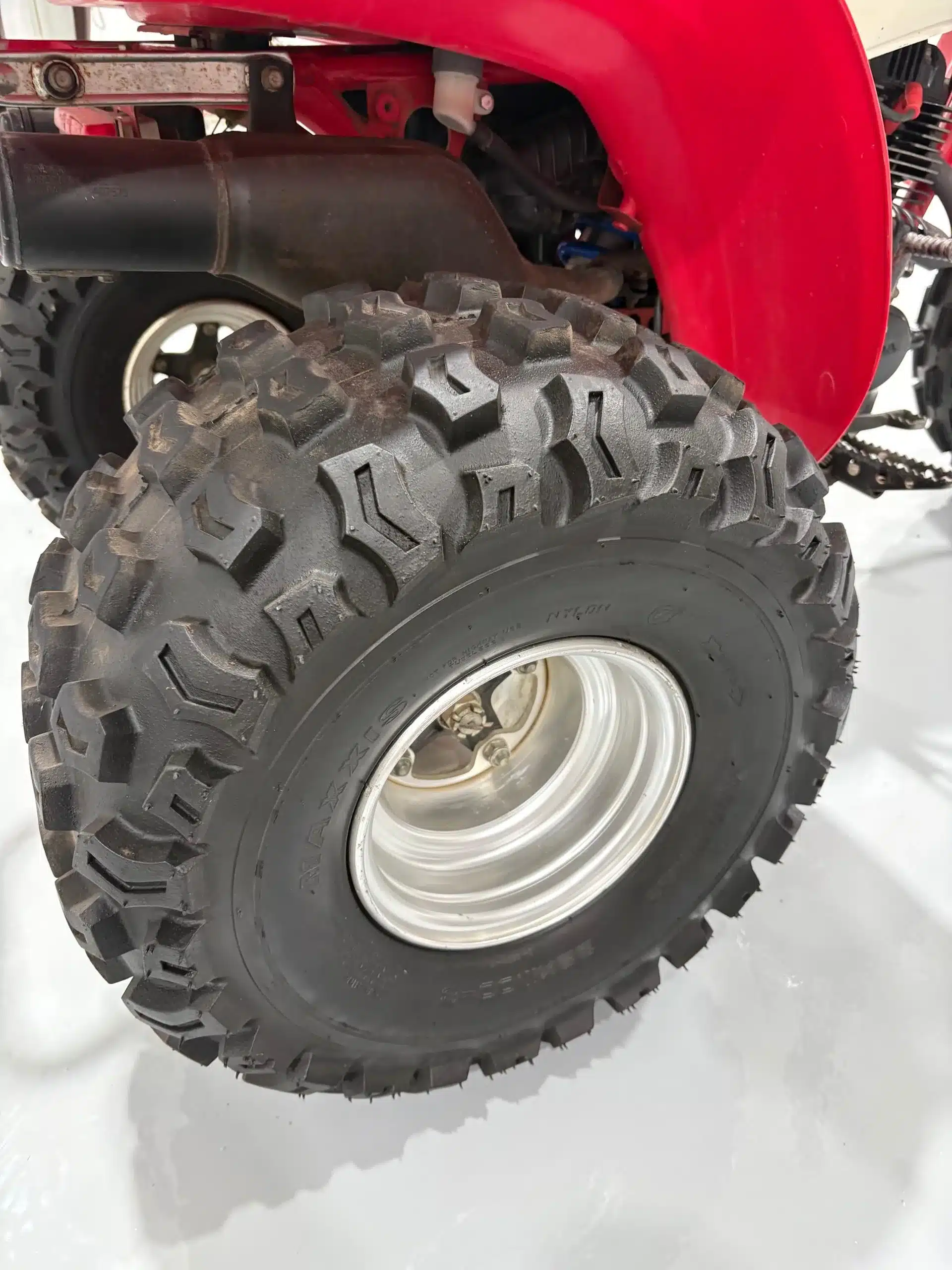 Nahaufnahme des grobstolligen Hinterreifens einer Honda ATC 200X mit Auspuff und rotem Kotflügel