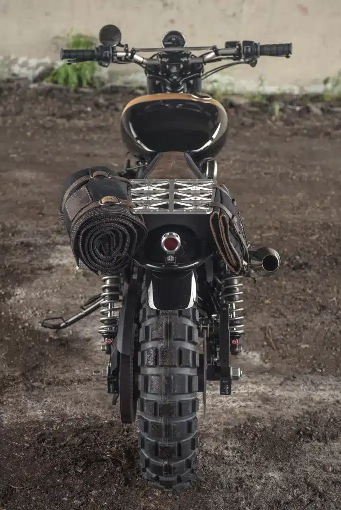 Heckansicht der umgebauten Harley-Davidson Street 750 als Scrambler, grobstolliger Hinterreifen, Gepäckträger und Adventure-Ausrüstung auf losem Untergrund.