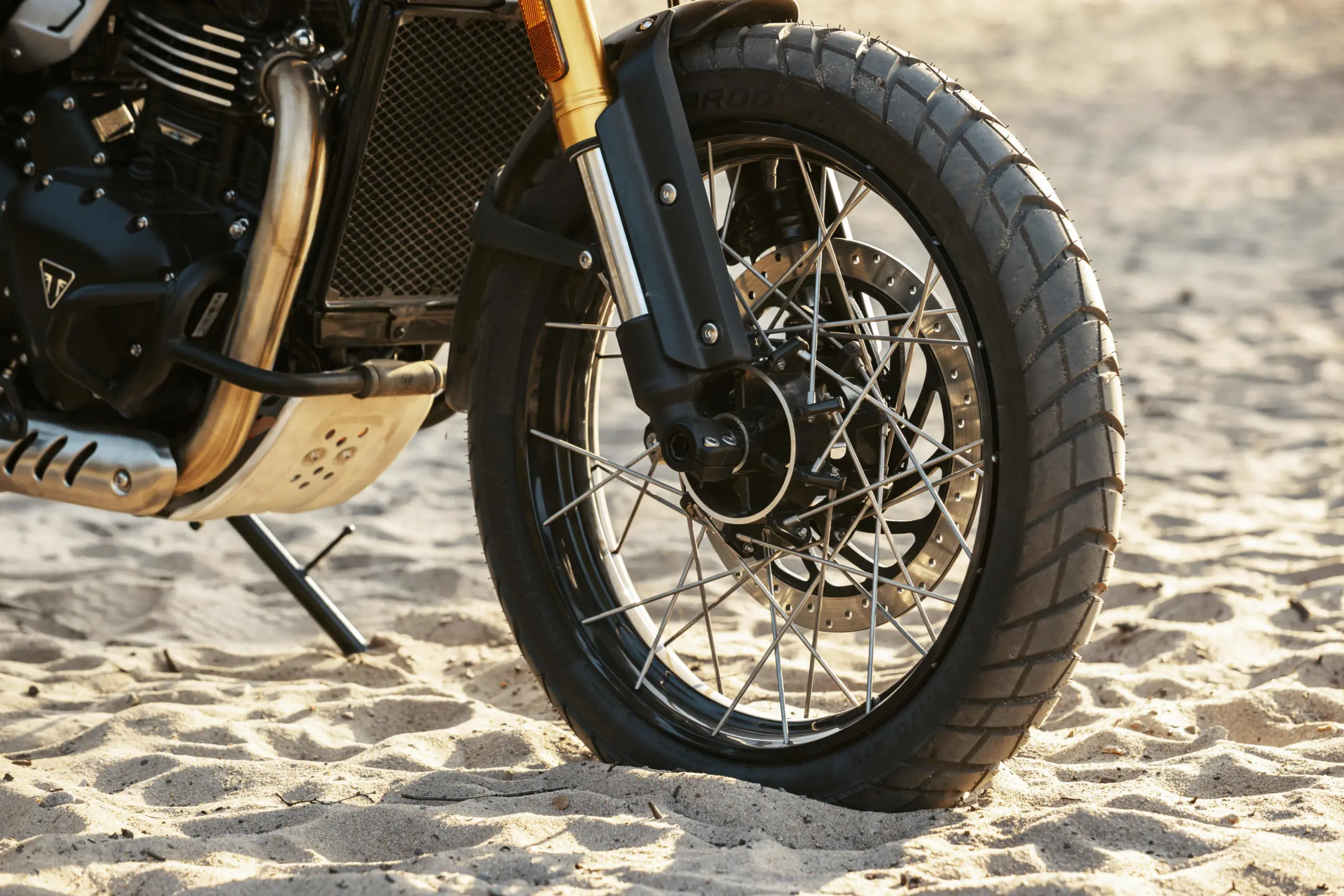 Vorderes Speichenrad einer Triumph Scrambler 400 XC mit grobstolligem Reifen im Sand.