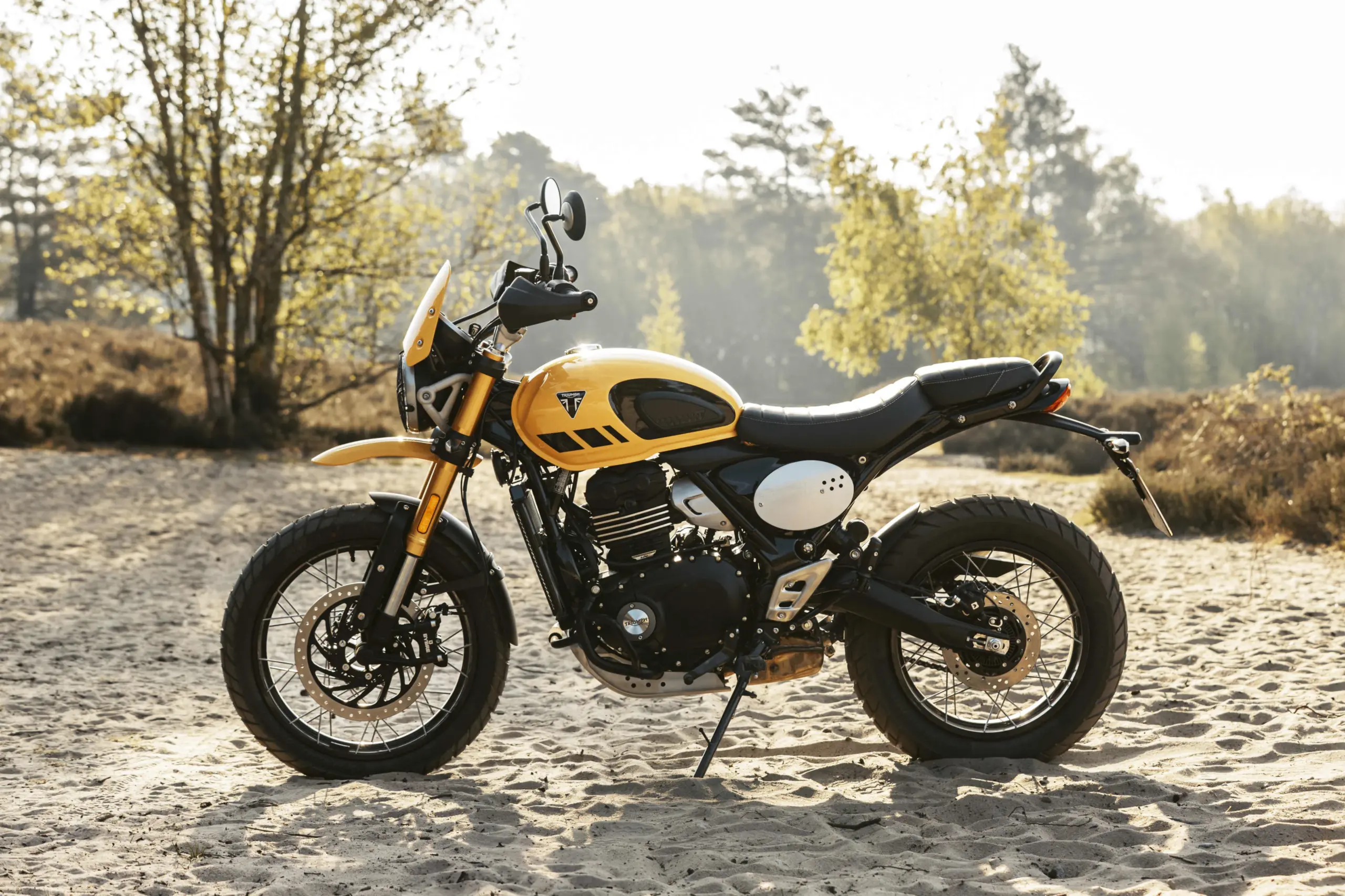 Seitenansicht der Triumph Scrambler 400 XC im Gelände mit gelbem Tank, Doppelauspuff und Speichenrädern.