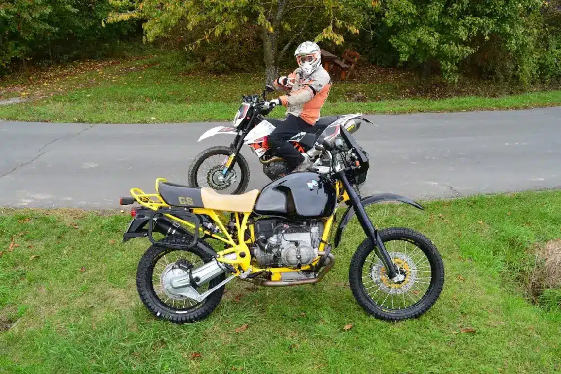 SWT-SPORTS BMW GS Boxer Umbau mit gelbem Rahmen und modernem Fahrwerk auf einer Wiese, im Hintergrund eine Enduro und ein Fahrer mit Helm